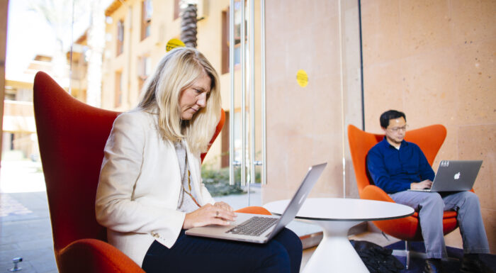 Professionals working on laptops in a modern lounge area at Stanford Graduate School of Business.