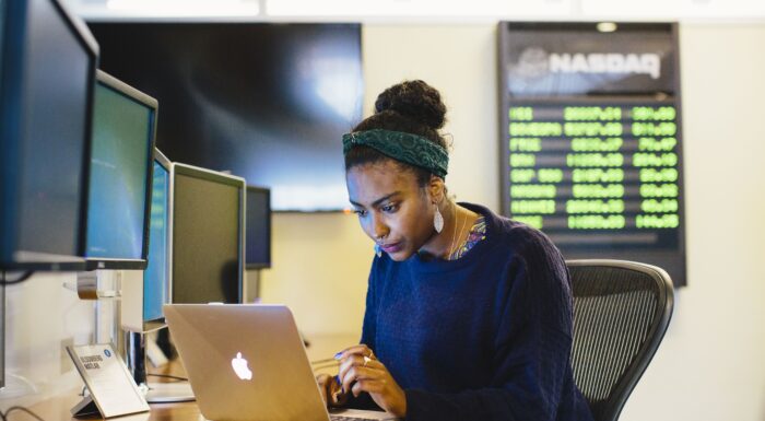 African-American woman researching on Apple Macbook in classroom.
